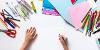 Child holding a pen about to draw surrounded by coloured pens and pencils