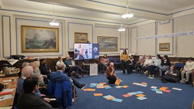 A group sat round talking about climate change with a man sat organising papers in the middle of the room.