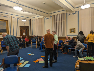 A room full of people with two men talking in the centre of the room.