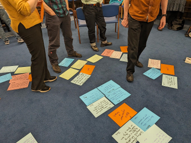 Sheets of paper on the floor with peoples legs and feet.