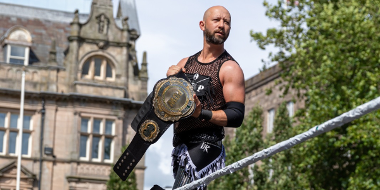 A wrestler stands in the ring holding a wrestling belt