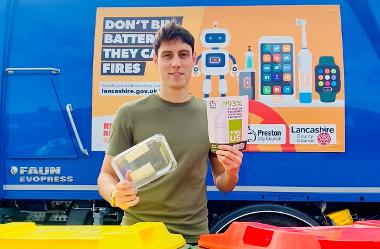 Freddie holding recycling campaign leaflet next to recycling bins