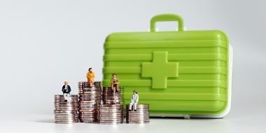 Old age miniatures sitting on a pile of coins with a medical kit.