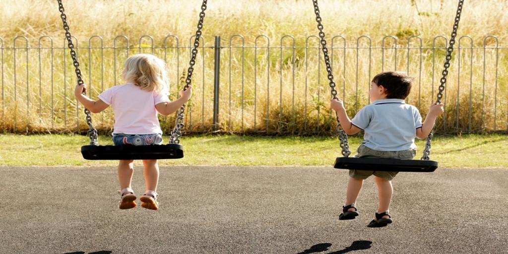 In a sunlit playground, two children find joy swinging together. The gentle breeze ruffles their hair as they soar back and forth, lost in the delight of carefree childhood moments.