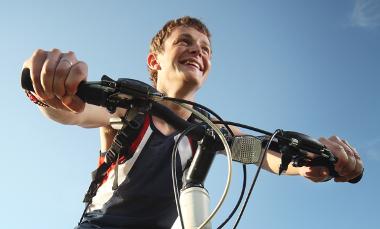 A smiling boy sat on his bike with a blue sky background